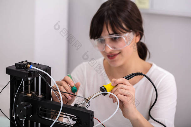 使用焊接铁佩戴安全眼镜的年轻女性技术员