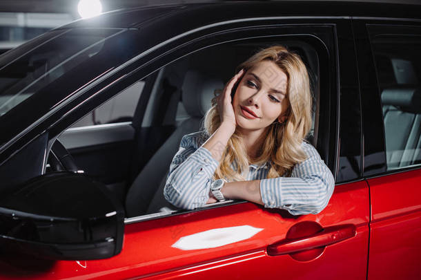 美丽的年轻女子坐在红色汽车在汽车陈列室
