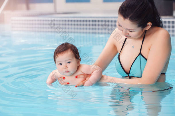混血亚洲母亲训练教她刚出生的宝宝漂浮在游泳池里。婴儿在水中潜水。健康积极的生活方式。家庭活动和早期发展概念