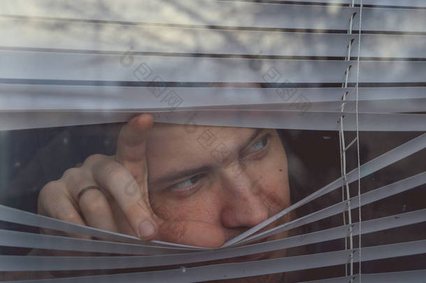 人透过百叶窗观看。有一双棕色眼睛透过窗户凝视着的多愁善感的年轻男性的画像