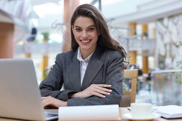 一个快乐的年轻女商人坐在办公室桌子边看着相机的画像.