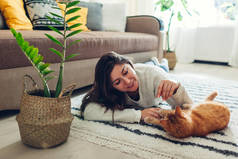 年轻的女人在家里的地毯上和猫玩耍。 主人和她的宠物躺在地板上