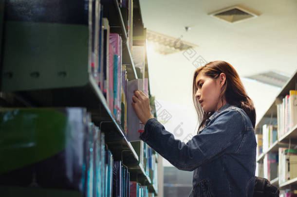 亚洲学生在国际学院/大学图书馆的书架上寻找课本。为大学考试的问题找到正确答案.