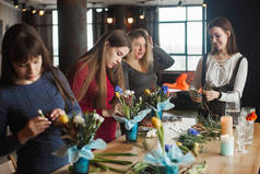 女性在植物学硕士班。 年轻的女士在做花卉作曲。 一群女性，在阁楼后面的室内开着花。 装饰过程.