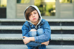 悲伤的男孩在上学前坐在楼梯上。独自不幸的孩子在城市街道.