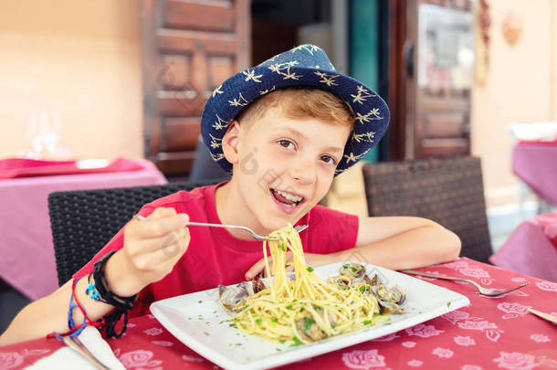 快乐的小男孩享受吃意大利食品 - 快乐微笑的孩子吃海鲜意大利面午餐和看相机的肖像 - 快乐的孩子在户外餐厅露台吃午饭