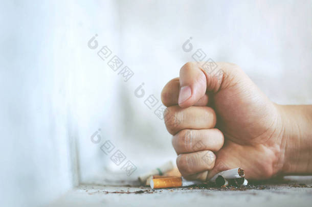 人手拳摧毁打破拒绝香烟。戒烟和健康的生活方式的概念。烟头在混凝土地板上，光水泥.
