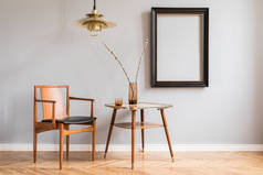 时尚明亮的复古内饰与设计椅子，金灯和小桌子与花瓶。灰色背景墙上的黑色模拟框架。客厅的简约概念。真实照片.