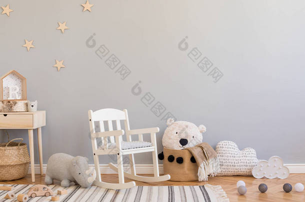 时尚和现代的斯堪的纳维亚新生儿内饰，配有玩具、儿童椅、毛绒犀牛、带泰迪熊的天然篮子和小木架。灰色背景墙，带星形图案.