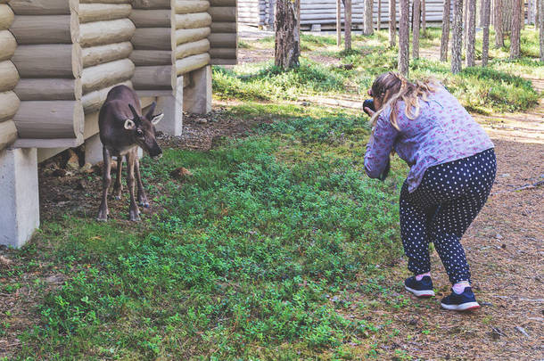 一个女孩在木屋附近照着一只鹿的照片
