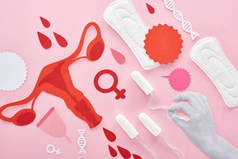 裁剪视图的白手拿着棉布在粉红色背景与卫生巾，剪纸女性生殖内脏器官和血滴