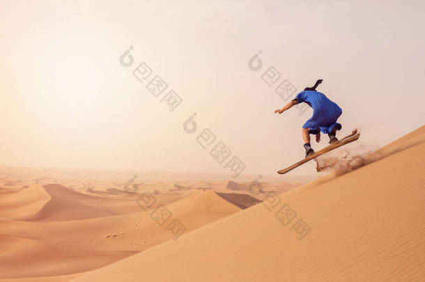 在摩洛哥埃尔格切加<strong>加沙</strong>丘上骑沙板时，身着图阿雷格·甘杜拉服装的沙板运动员的后视图表演跳跃技巧