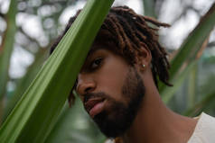 胡子青年戴耳环在棕榈树附近摆姿势