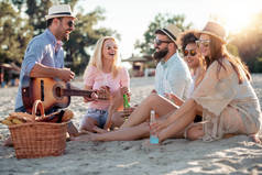 一群朋友在沙滩上听吉他和喝啤酒.