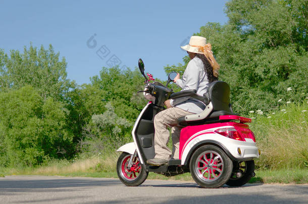 一个戴着太阳眼镜、戴着帽子的非洲裔美国妇女骑着电动滑板车的肖像。在夏季，在绿色城市公园内自由乘坐<strong>机动车</strong>辆.
