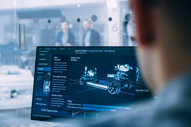 专业工程师使用 3d Cad 软件在计算机上工作，并在高科技开发实验室中测试电动汽车底盘原型，并配有车轮、电池和发动机.