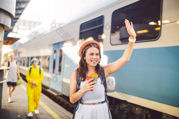 背包旅客妇女挥手在火车站站台暑假旅游的概念。女性游客问候和享受在火车上，旅行的概念。主题交通和旅行