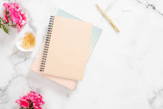 空白纸笔记本，粉红色的花朵，大理石背景的金色文具。平躺，顶视图女性家庭办公桌.