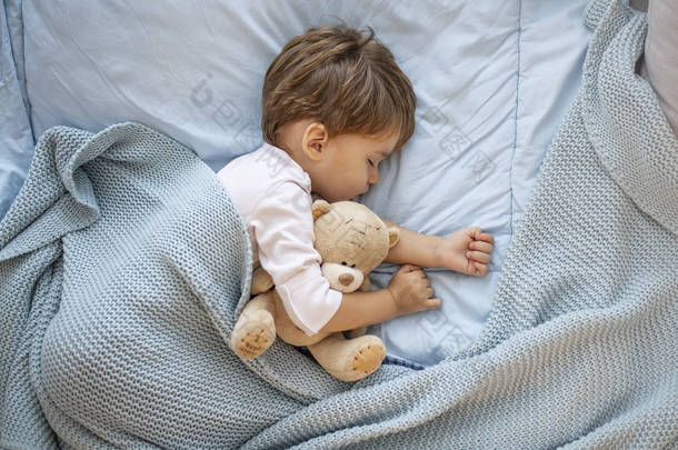 男婴与泰迪熊睡在一起的照片。他最喜欢的午睡点。可爱的男孩睡在床上与玩具后。男孩睡在床上与泰迪熊。懒虫