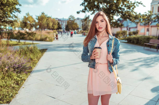美丽的女学生站在城市的夏天，拿着一杯咖啡茶，黄色的手提包，等待朋友的女朋友，<strong>长长</strong>的头发，晒黑了苗条的身材。 粉红色的衣服是随意化妆的. 文件的自由篇幅.