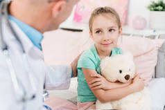在医务室听医生的建议时，带着毛绒玩具的可爱小女孩笑着看着她的医生