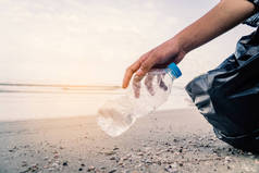 手拿起塑料瓶在海滩清洁，志愿的概念.