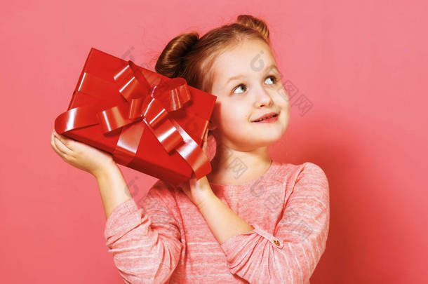 一个粉红背景上有一缕头发的小女孩的画像。 一个孩子手里拿着一个盒子，手里拿着礼物，在想，在幻想，在做梦