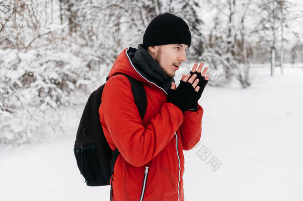 穿着黑帽和红羽衣的年轻人在冬日公园<strong>暖手</strong>