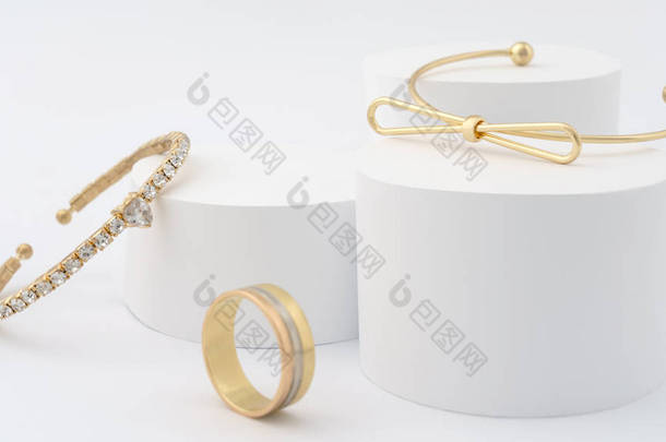 白色背景上的金手镯和金戒指。 白色平台上的现代设计金手镯和戒指.