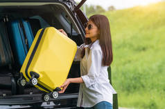 亚洲女人在旅行时将黄色的行李箱提上Suv车