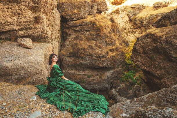 在哈萨克斯坦南部的阿克苏峡谷，身着郁郁葱葱绿色连衣裙的女人。穿着童话般晚<strong>礼服</strong>的年轻女子站在岩石和高山的背景上.在山里穿<strong>长裙</strong>的漂亮姑娘
