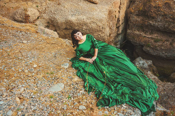 在哈萨克斯坦南部的阿克苏峡谷，身着郁郁葱葱绿色连衣裙的女人。穿着童话般晚礼服的年轻女子站在岩石和高山的背景上.在山里穿长裙的漂亮姑娘