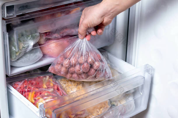 男人把装有肉丸子的塑料袋放进冰箱，里面装着冷冻蔬菜，特写镜头