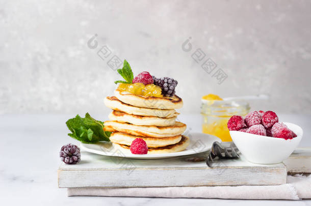 自制的煎饼加果酱,冰冻的覆盆子,黑莓和薄荷糖放在木板上.浅灰背景。早餐.