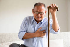 亚洲老人坐在沙发上，心疼，在家里心脏病发作。高级保健概念.