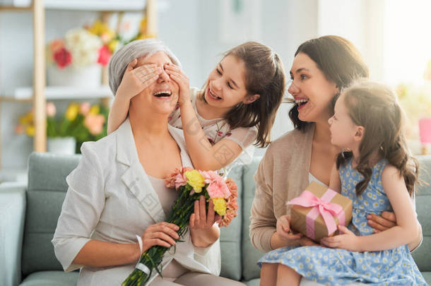 母亲节快乐！孩子们的女儿们在祝贺妈妈和奶奶送给她们鲜花和礼物。奶奶，妈妈和女孩们笑着拥抱。家庭假日和团聚.