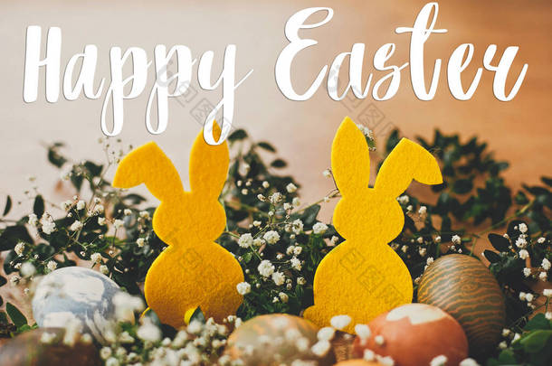 复活节快乐短信复活节贺卡。时尚的复活节彩蛋，黄色的兔子在春天花朵的窝在乡村木桌上。天然染色的复活节彩蛋和兔子.假日卡片