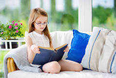 小女孩在客厅里看书。聪明的女学生放学后做作业.儿童的教育和远距离学习。检疫期间在家学习。待在家里娱乐.