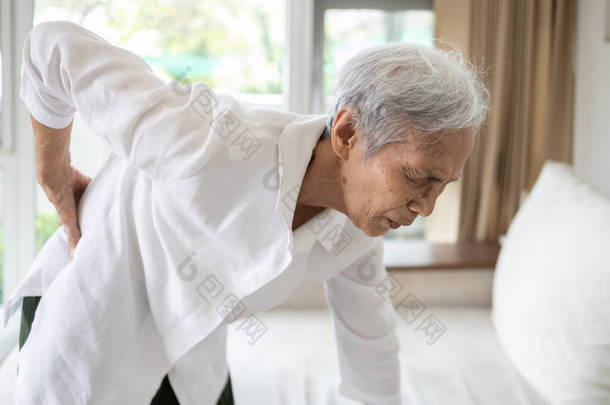 悲伤的亚洲老年妇女，站立时背部和髋关节疼痛，女性患者背痛，腰痛，手摸髋部，老年人肋骨受伤或腰痛，健康问题