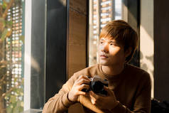 身着休闲装的亚洲男性专业摄影师在橱窗边的咖啡店内挑选相机滤镜，并观看照片