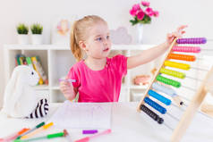 一个金发碧眼的小女孩坐在白色的书桌前，指望着教室里五颜六色的算盘。3.学前教育