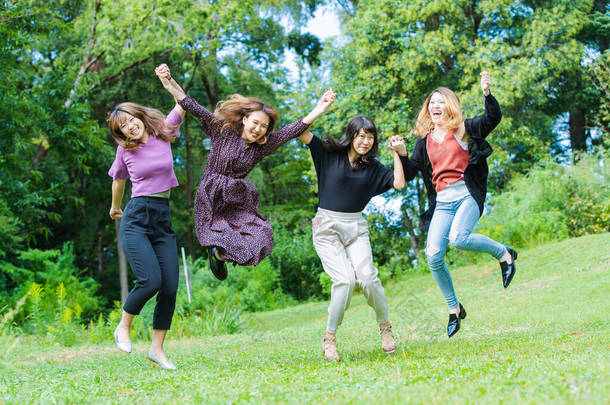 四名亚洲年轻女子在公园里笑着跳了起来