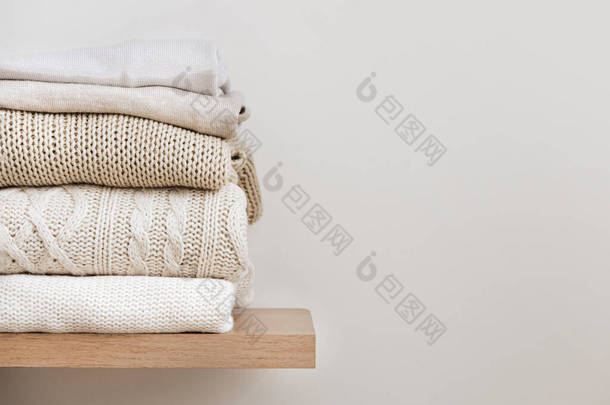 一堆叠得整整齐齐的温暖针织品，放在木制架子上的羊毛和米色的背景。采购产品胶囊衣橱，衣服储存，<strong>简约</strong>主义，针织纹理，秩序，舒适。带有文本复制空间的横幅.