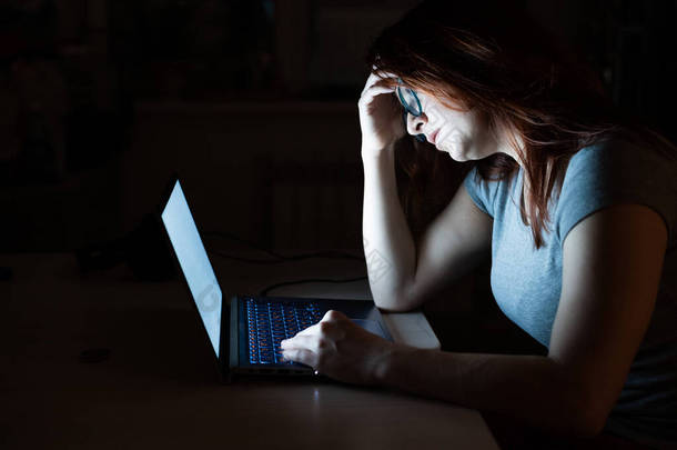一个女人<strong>加班</strong>。一个晚上在黑暗中在笔记本电脑前学习的学生。3.这个女孩为工作中的问题忧心忡忡，双手插在额头上.