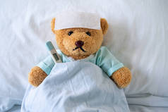 病熊穿着耐穿的衣服.躺在床上发高烧，额头上和温室里放着一种退热凝胶，放在腋下