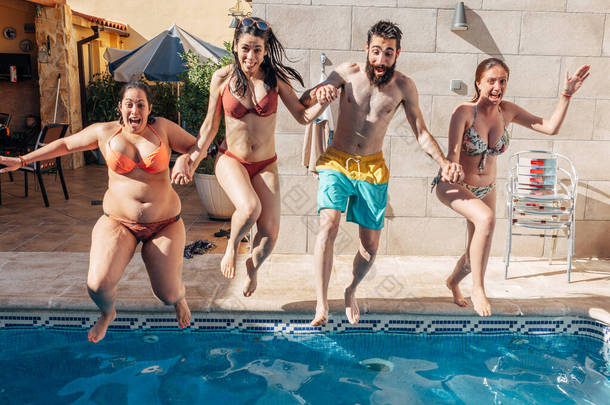 一群快乐的朋友牵着手跳进游泳池。年轻的多元文化人士在度假时很开心.假日、青年和友谊概念