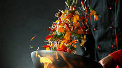 厨师用火锅把蔬菜调料倒入锅中.深色背景下的亚洲新鲜食品.