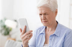 近视概念。上了年纪的女人斜视着智能手机屏幕