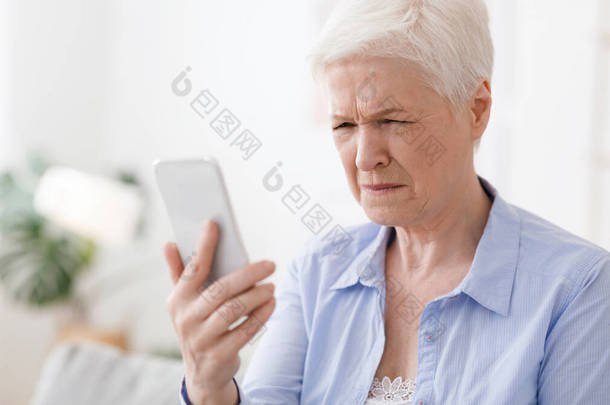 <strong>近视</strong>概念。上了年纪的女人斜视着智能手机屏幕