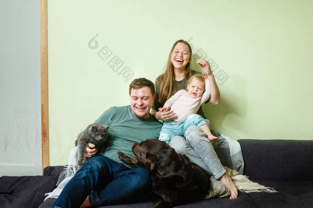 年轻快乐的家庭，带着小孩和宠物狗猫呆在沙发上，呆在家里的观念，身强体壮，人见人爱